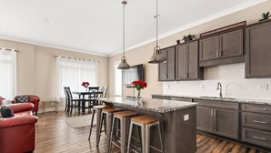 A modern kitchen with dark wooden cabinets, a granite countertop, and a dining area with a red leather couch and a table with red flowers.