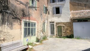 Un edificio de dos pisos con fachada de piedra, una puerta verde y una ventana con contraventanas.