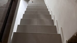 Una escalera moderna con barandilla de metal, paredes blancas y suelo de baldosas.