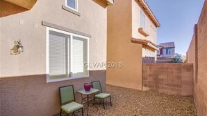 A small patio area with two chairs and a table, a window with blinds, and a brick wall. - Entire home in beautiful  Southwest Las Vegas, NV area! (Las Vegas)