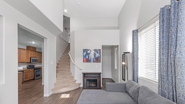 A modern living room with a gray sectional sofa, a fireplace, and a staircase leading to a kitchen with wooden cabinets and a microwave. - Entire home in beautiful  Southwest Las Vegas, NV area! (Las Vegas)