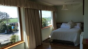 Une chambre à coucher avec un lit, une fenêtre avec des rideaux, une table de chevet et une vue sur l’extérieur.