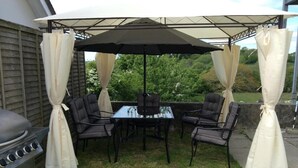 Une terrasse extérieure équipée d’un barbecue, d’une table à manger et de chaises, le tout abrité par un auvent.