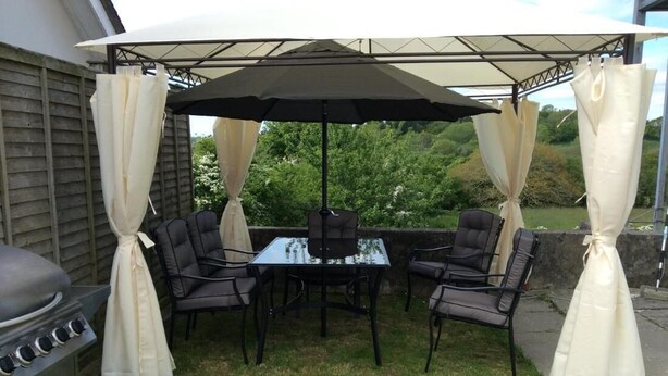 Une terrasse extérieure équipée d’un barbecue, d’une table à manger et de chaises, le tout abrité par un auvent.
