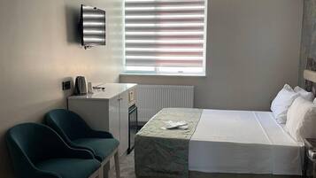 A small, neatly arranged bedroom with a bed, two chairs, a desk, and a radiator.