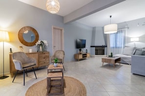 A modern living room with a sofa, armchair, coffee table, TV, fireplace, and a large mirror.