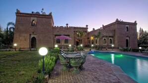 A courtyard with a swimming pool, outdoor seating, and a large building with arched windows and a tower. - Palace With 2 Villas and 2 Swimming Pools in Sidi Abdellah Ghiat (Sidi Abdallah Ghiat)