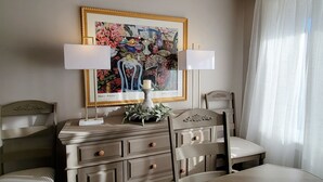 Ein Schlafzimmer mit Bett, Kommode mit Schubladen, Stuhl, Tisch, Lampe und einem gerahmten Kunstwerk an der Wand.