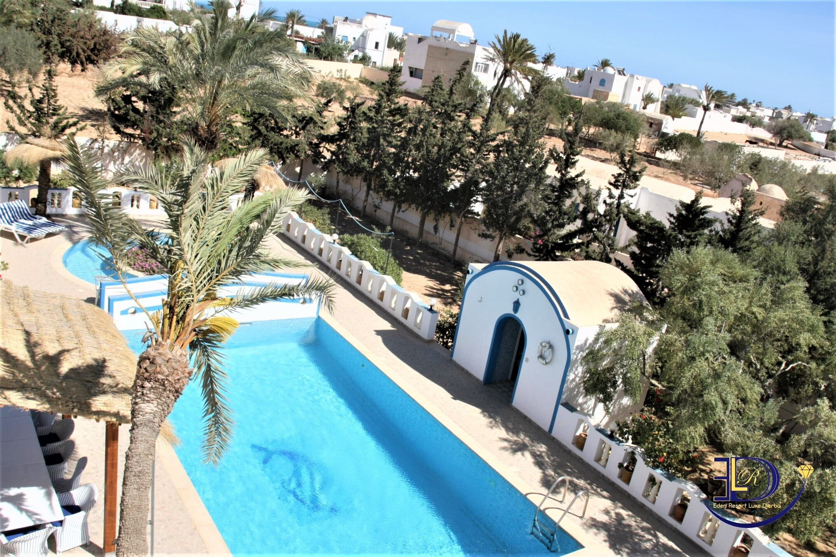 A resort with a swimming pool, palm trees, and a view of the surrounding buildings.