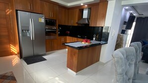 A modern kitchen with wooden cabinets, a stainless steel refrigerator, and a central island. - Fully Equipped Apartment With sea View (Santo Domingo Este)