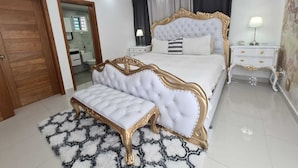 A bedroom with a large bed, a bedside table, a nightstand, a bench, and a door. - Fully Equipped Apartment With sea View (Santo Domingo Este)