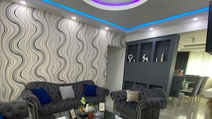 A modern living room with grey sofas, a glass coffee table, and a wavy patterned wall. - Fully Equipped Apartment With sea View (Santo Domingo Este)