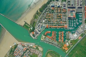 An aerial view of a coastal marina with multiple docks, a beach, and residential buildings.