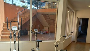 Uma academia com equipamentos de ginástica, janelas amplas e vista para escadas externas.