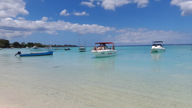 Ein Strand mit klarem türkisblauem Wasser, Booten und einem Sandstrand.