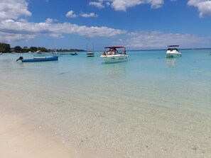 Ein Strand mit klarem türkisblauem Wasser, Booten und einem sandigen Ufer.
