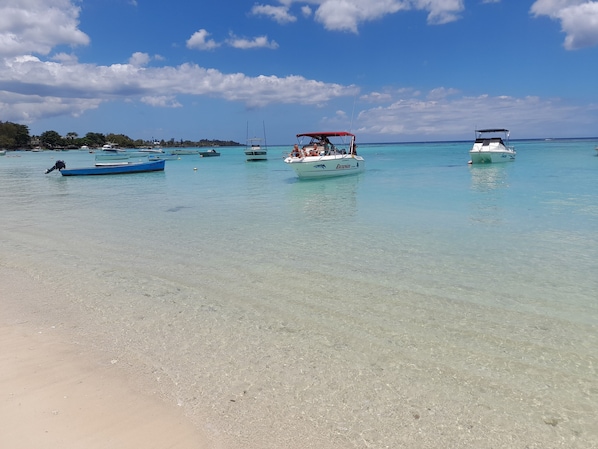 A beach with clear turquoise water, boats, and a sandy shore.