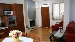 Ein Wohnzimmer mit Kamin, einem Esstisch mit Blumenvase, einem roten Sofa und einem Couchtisch.