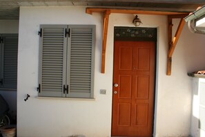 A wooden door with a small window above it, a light fixture above the door, and a wall-mounted light switch. - La Taverna di Sophie (Rapolano Terme)
