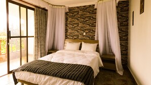 A bedroom with a large bed, a stone wall, and a balcony with curtains.