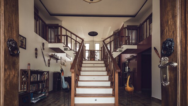 A grand staircase with wooden railings and a chandelier, leading to a second floor with a view of the outdoors.