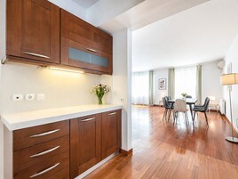 A modern kitchen with wooden cabinets, a white countertop, and a dining area with a table and chairs.