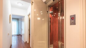 A hallway with a wooden floor, a door leading to an elevator, and a light switch on the wall. - Adelos III Bloom Villa 5BR 360m² - Sauna - Rooftop (Elliniko-Argyroupoli)