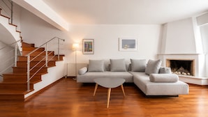 A modern living room with a wooden staircase, a grey sofa set, a small coffee table, and a fireplace. - Adelos III Bloom Villa 5BR 360m² - Sauna - Rooftop (Elliniko-Argyroupoli)