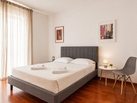 Habitación de hotel moderna con una cama, una silla, una mesita y dos cuadros en la pared.