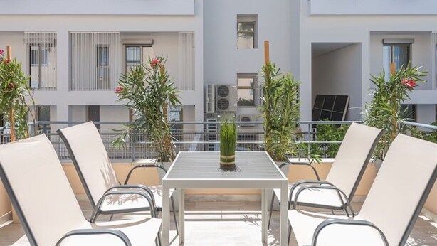 A balcony with a table and chairs, surrounded by potted plants. - Adelos III Bloom Villa 5BR 360m² - Sauna - Rooftop (Elliniko-Argyroupoli)