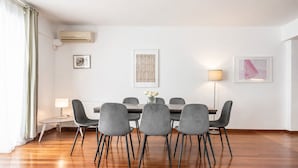 A dining area with a wooden table and grey chairs, a small side table with a lamp, and artwork on the walls. - Adelos III Bloom Villa 5BR 360m² - Sauna - Rooftop (Elliniko-Argyroupoli)