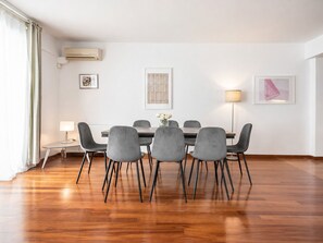 A dining area with a wooden table and grey chairs, a small side table with a lamp, and artwork on the walls. - Adelos III Bloom Villa 5BR 360m² - Sauna - Rooftop (Elliniko-Argyroupoli)