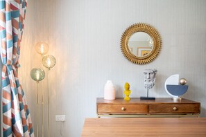 Een kamer met een houten dressoir, een spiegel met een zonvormige lijst, en een vaas op het dressoir.