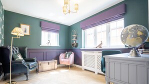 A room with a herringbone floor, a black leather armchair, a pink chair, a globe on a desk, and a window with a view of a bird. - Comfortable 5 Bedroom Detached House With Parking (Bicester)