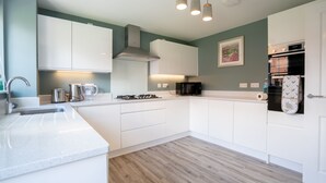 A modern kitchen with white cabinets, a stainless steel sink, and a built-in oven. - Comfortable 5 Bedroom Detached House With Parking (Bicester)
