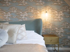 A bedroom with a bed, pillows, a nightstand, and a wall with a cloud pattern. - Comfortable 5 Bedroom Detached House With Parking (Bicester)