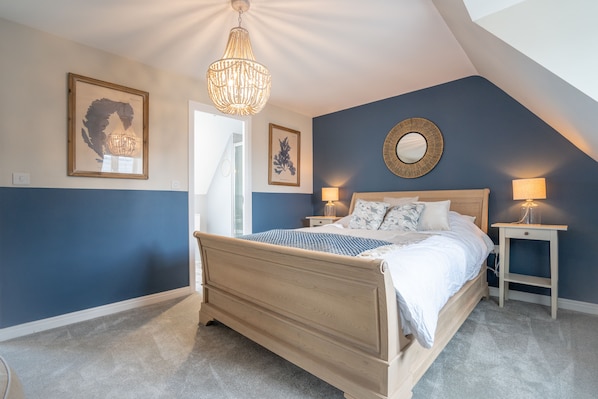 Een slaapkamer met een bed, nachtkastjes, een kroonluchter, lijstwerk en een dakvenster.