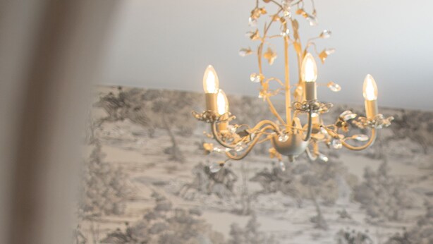 A bedroom with a tufted headboard, a chandelier, and a patterned wallpaper. - Comfortable 5 Bedroom Detached House With Parking (Bicester)