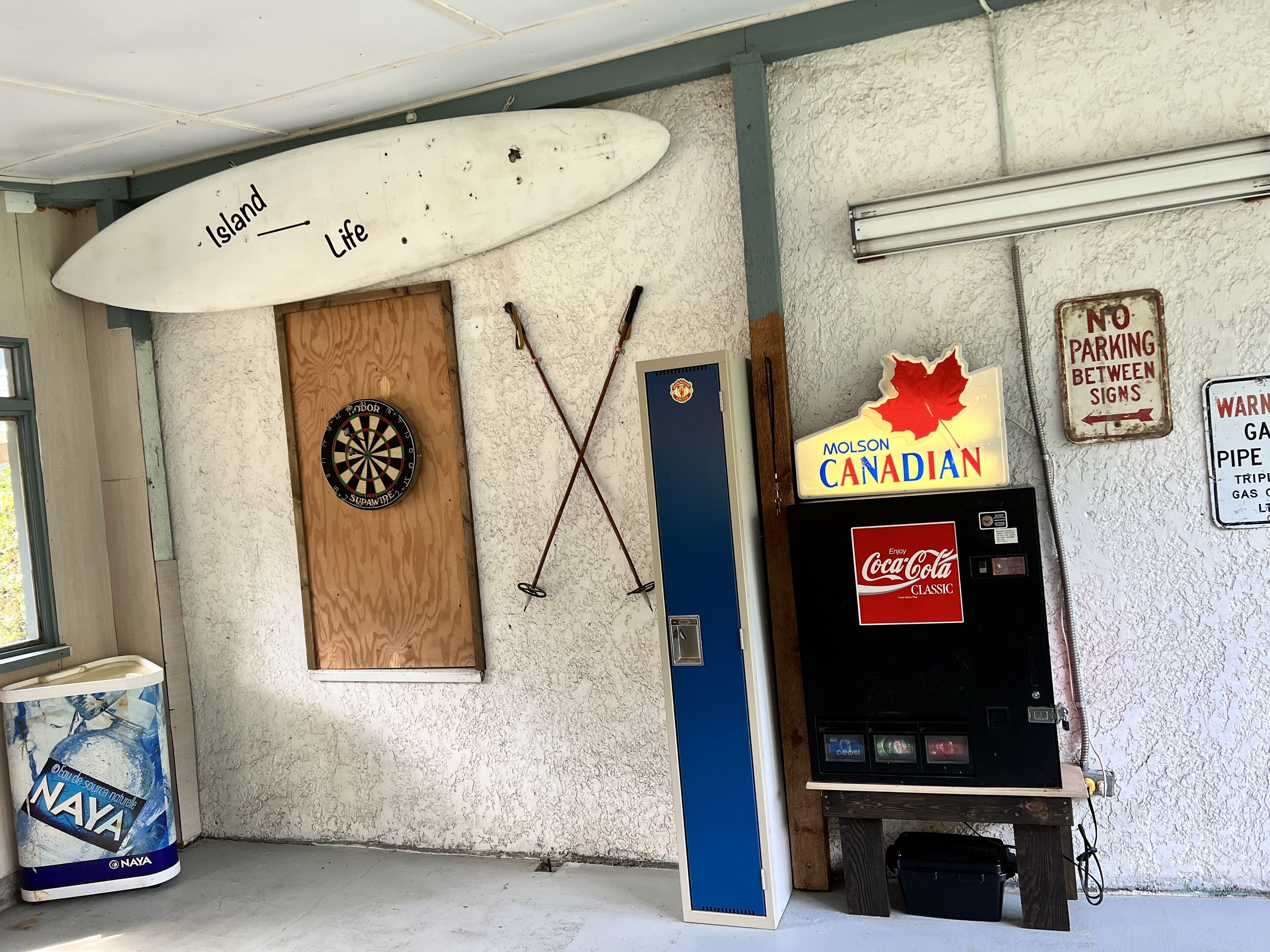 Une pièce équipée d’un jeu de fléchettes, d’une planche de surf, d’un réfrigérateur et d’un distributeur automatique.
