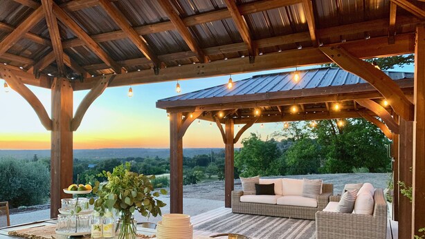 Eine Terrasse im Freien mit einer Holz-Pergola, Korbmöbeln und Lichterketten.