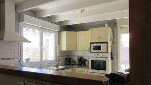 Una cocina con armarios de colores claros, microondas, horno y una ventana con cortinas.
