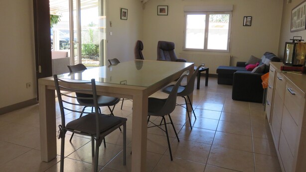 Un amplio espacio de sala con una mesa de comedor de vidrio, asientos cómodos, un sofá y una zona de cocina.