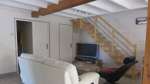 Una sala de estar con un sofá blanco, un televisor, una escalera de madera y un cartel que indica una habitación para bebés.