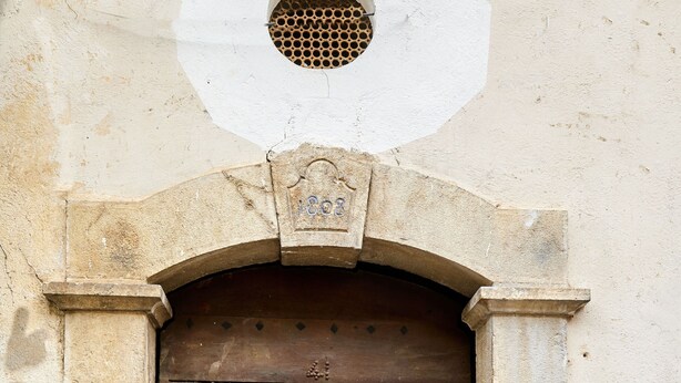 Una puerta de madera desgastada con un tirador de metal, enmarcada en un arco de piedra.