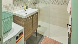 Un baño moderno con cabina de ducha de vidrio, un lavabo con espejo y una cesta verde.
