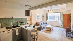 Una cocina moderna con una isla central, un comedor con sofá y mesa, y un ventanal con cortinas.