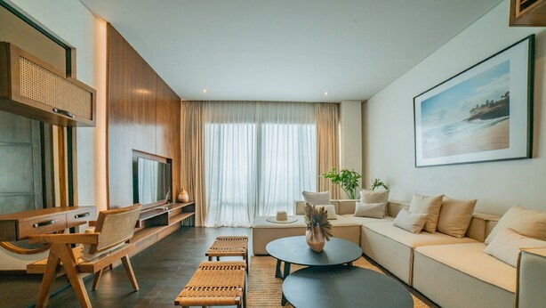 A modern living room with a sofa, two round coffee tables, a TV, and a large window with sheer curtains. - Apartment Seabreeze 1 (Canggu)