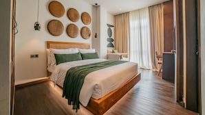 A modern bedroom with a wooden bed, a green throw blanket, and woven wall art. - Apartment Seabreeze 1 (Canggu)
