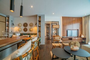 A modern living room with a wooden dining table, chairs, a TV, and a bookshelf.