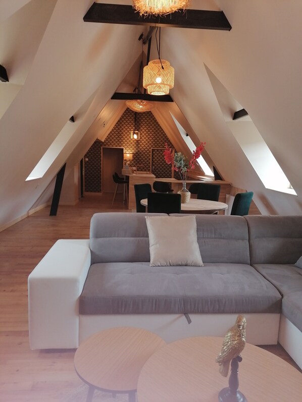 Ein modernes Loft mit geneigter Decke, einem grauen Ecksofa, einem runden Holztisch und einem Essbereich mit Stühlen.